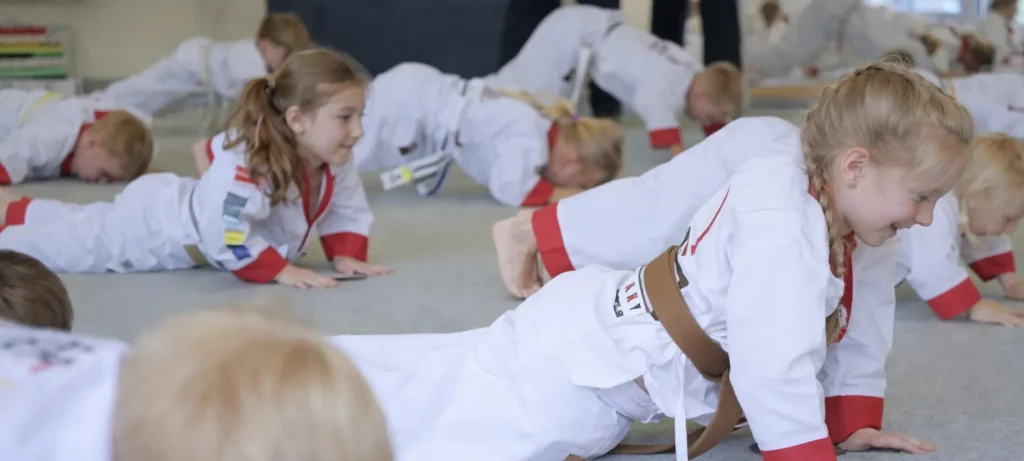 Junge Taekwondo-Schüler in weißen Anzügen machen Liegestütze auf einer Dojo-Matte während des Trainings.