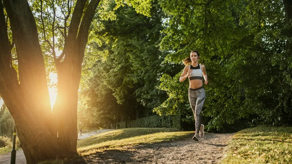Frau joggt im Park und zeigt, wie Bewegung Gesundheit, Ausdauer und mentale Stärke positiv unterstützt