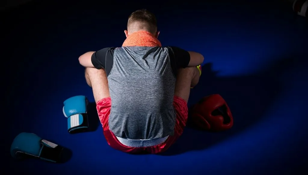 Erschöpfter Kampfsportler sitzt zwischen Handschuhen am Boden, passend zum Thema Unternehmer-Burnout vermeiden